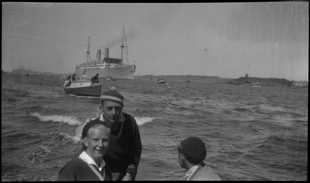 Finn Johannessen, J. Jensen, Harald Bergsaker og Ottar Roaldsøy på seiltur i Byfjorden, ved Stavanger. I bakgrunnen er et stort dampskip ledsgket av et mindre dampskip, begge med vimplene oppe, og mange småbåter.