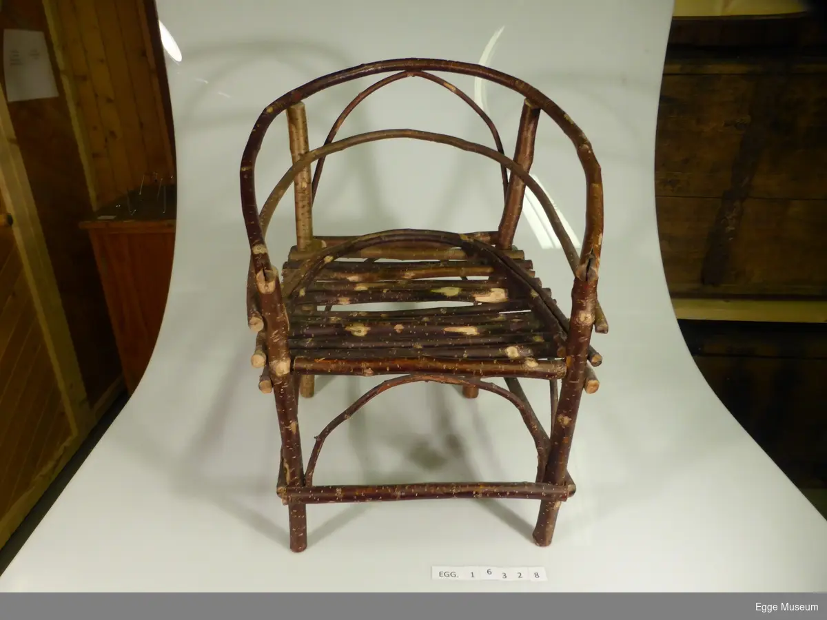 Barnestol konstruert av trekvister av ulike løvtresorter som er spikret sammen. Form: firkantet sete med to buede støttekvister. Fire bein. Buet rygg som går over i armlener. Stolen ble laget under krigen.