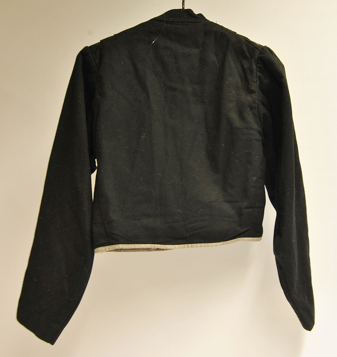 Kort jakke. Tilhørende folkedrakt. Mulig laget til en brud. Rad med sort blonde ned på hver side av brystet. Meget for seg gjort.