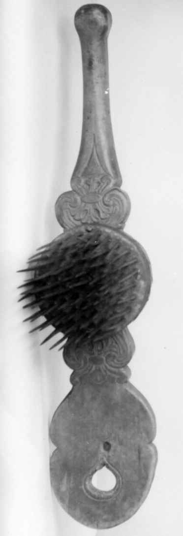 Linhekle av tre der den ene enden er flat og avrundet, mens den andre enden er avlang og rund. På midten er det festet en rundt metallskive med stålnagler. Linheklen er dekorert med utskjæringer.