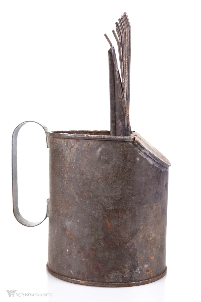 Sylinderformet blikkboks som kropp, med påloddet buehåndtak og en skråstilt plate med tenner foran.