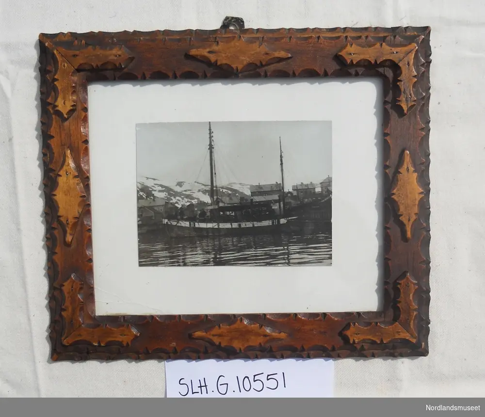 Foto av seilskøyta "Hilda" montert i ramme med treutskjæringer.