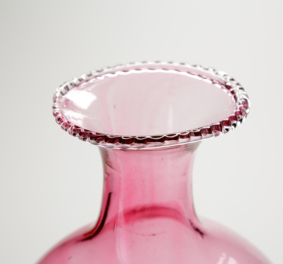 Vas eller pokal.
Stilen på glasen är gjord så att den ska se ålderdomlig ut.
Hög rosa vas/pokal som vidgar sig uppåt, och avslutas i en smal hals med utvikt mynning. På mynningen en ofärgad och naggad glastråd.
Benet är ofärgat och utgörs av tre vulster.  
Foten rosa.