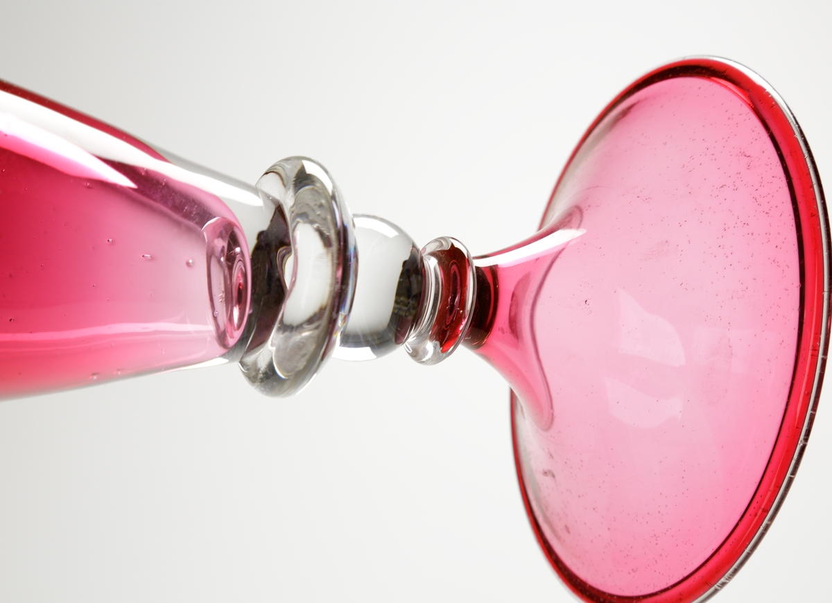Vas eller pokal.
Stilen på glasen är gjord så att den ska se ålderdomlig ut.
Hög rosa vas/pokal som vidgar sig uppåt, och avslutas i en smal hals med utvikt mynning. På mynningen en ofärgad och naggad glastråd.
Benet är ofärgat och utgörs av tre vulster.  
Foten rosa.