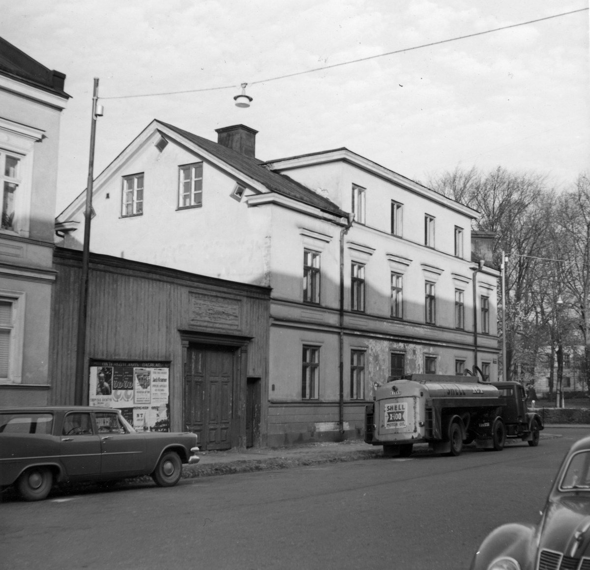Vy mot Prästgatan 49. Djäkneparkskolan skymtar bakom träden till höger. Gatan visar tidstypiska inslag som Östergötlands Dagblads anslagstavla, träporten in mot innergården och exempel på tidens tankbilsmodeller.