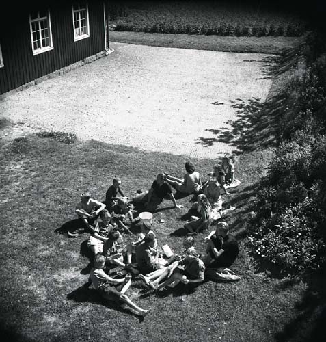 En gupp vuxna och barn sitter ute på gräset. Unga Odlare 1948 - 1949.