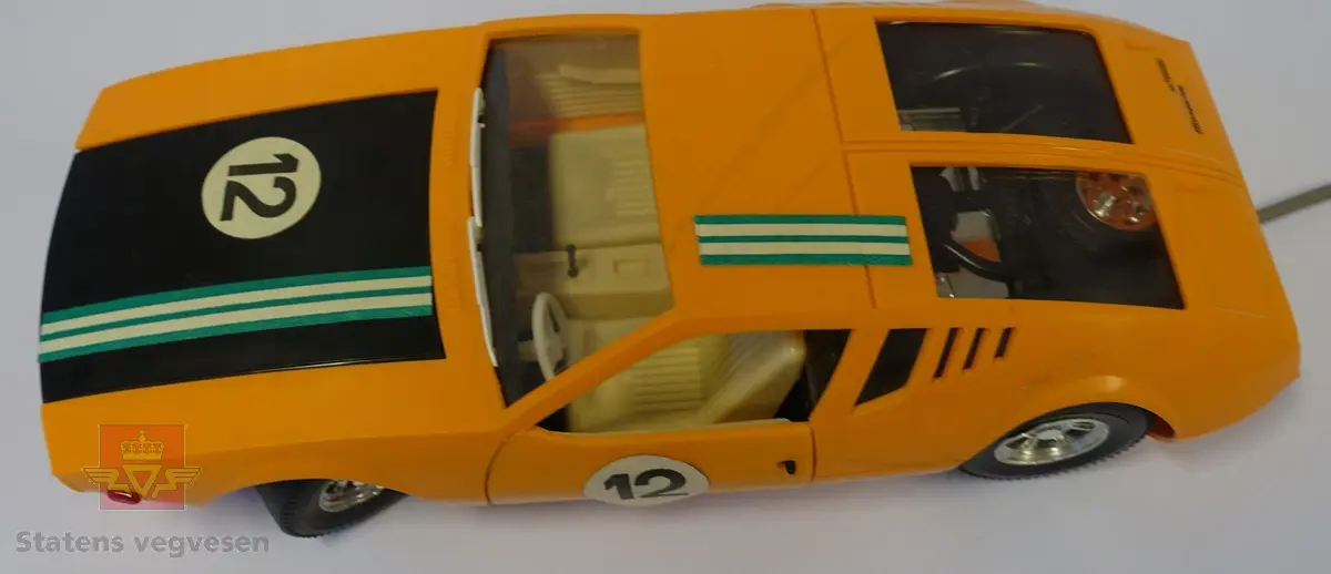 Miniatyr, lekebil i eske. Laget hovedsakelig av plast med eske av papp. Oransje bil i hvit eske med foto av bilen på. Skala 1:12. Batteridrevet fjernkontroll med ledning medfølger.