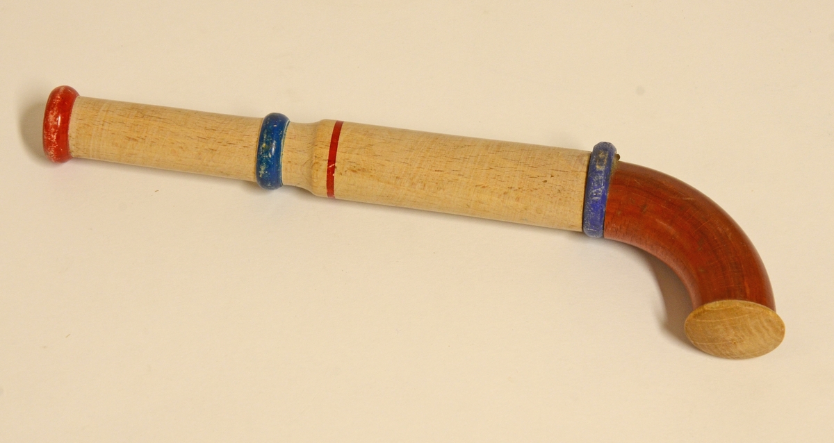 Leksakspistol som skjuter korkar av trä. Pistolen är delvis målad i brunt, blått och rött.