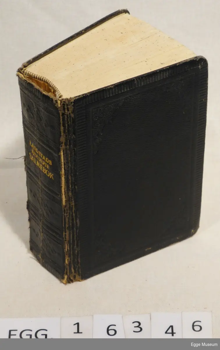 Rektangulær, svart salmebok med stive permer og innpreget mønster på omslaget og bokryggen. På bokryggen står "Landstads reviderte salmebok" trykket på med gullfarge.