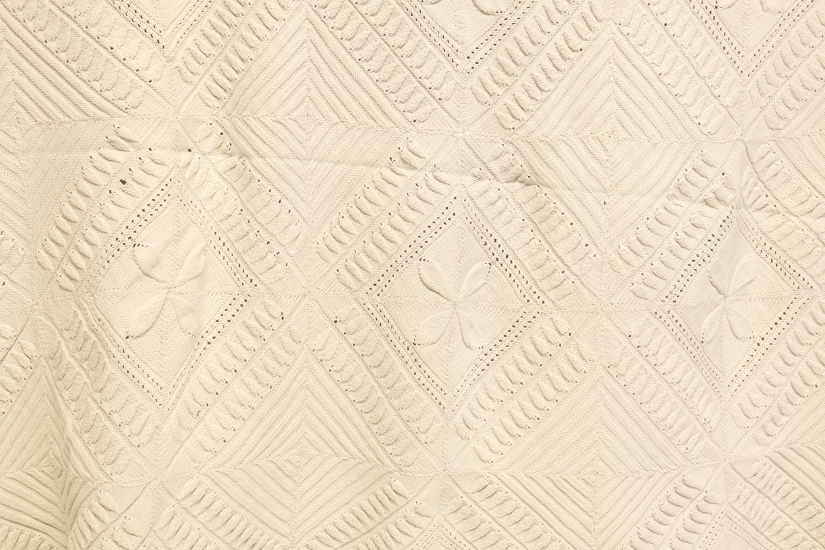 To strikkede sengetepper med frynser (a-b) og en nyere strikkeprøve med oppskrift (c). 
A) Sengeteppe i hvitt bomullsgarn satt sammen av 9x11 mindre lapper. Lappene er sydd sammen for hånd. 4 og 4 lapper danner et mønster. Strikkemønsteret har variert stolpemønster i rett og vrang.
B) Som a), men svært hullete og gulnet, og det er strikket med et tynnere bomullsgarn. Teppet består av 8x11 lapper.
C) Strikkeoppskrift med strikkeprøve/rekonstruksjon i beige bomullsgarn.