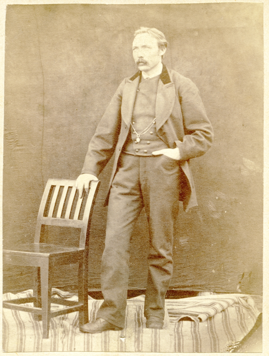 Portrett av mann stående ved en stol.