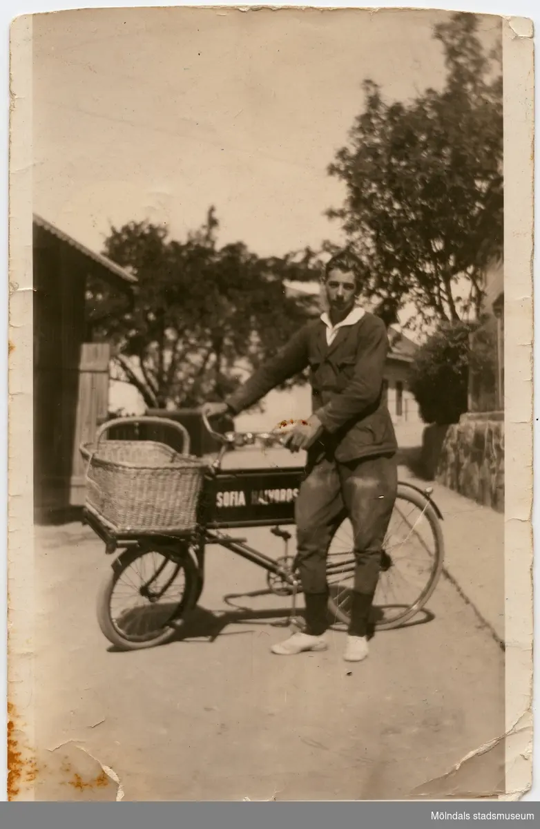 William Olsson, 1908 - 2001, med sin cykel i Mölndals Kvarnby, ca 1923-1924. William arbetade som springpojke för Asklunds bageri och för Sofia ”Soffi” Halvordsons bageri. Soffis bageri låg på Friareliden (nuvarande Samuel Norbergsgatan).