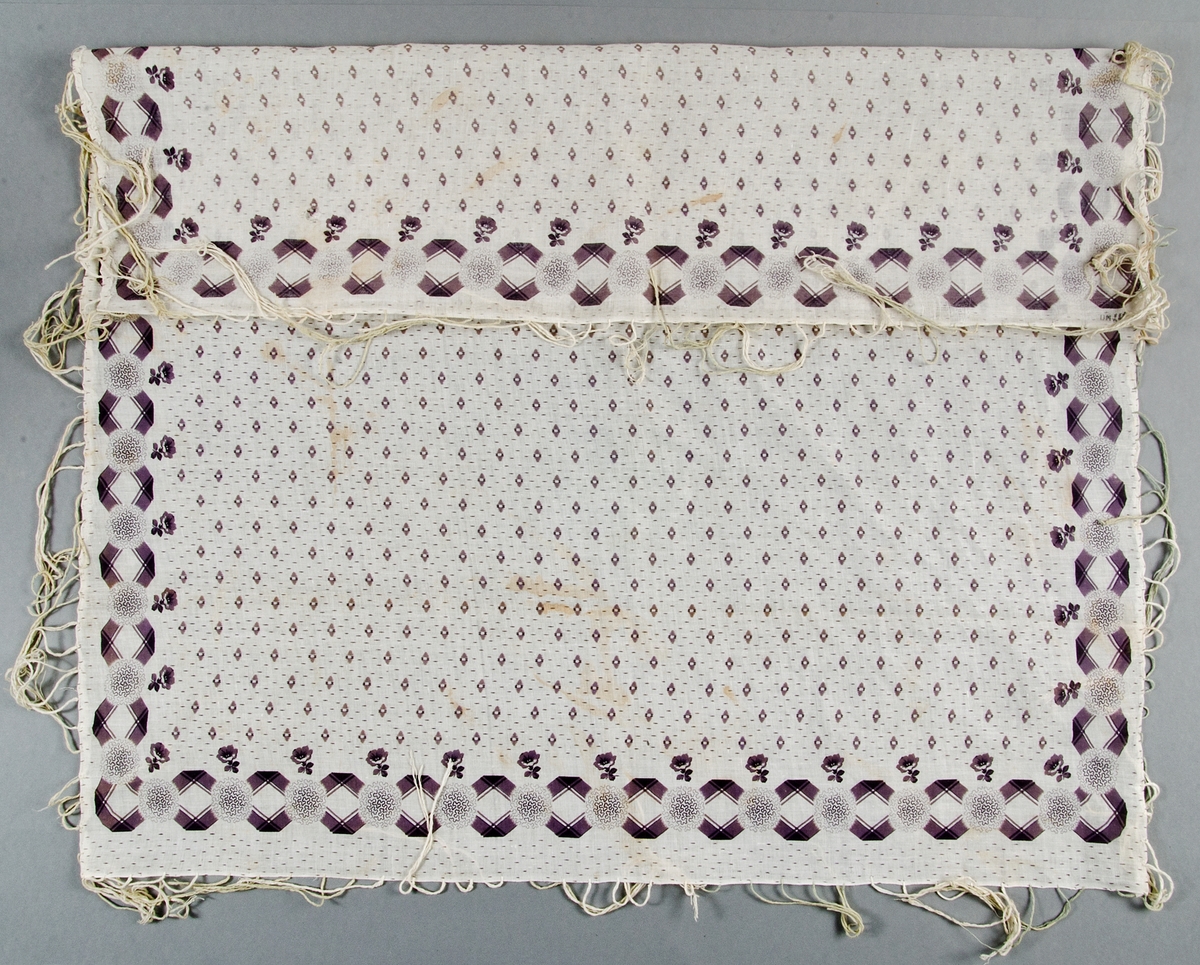 Kläde av maskinvävd vit bomullslärft med tryckt lila mönster. Iknutna fransar av bomullsgarn.