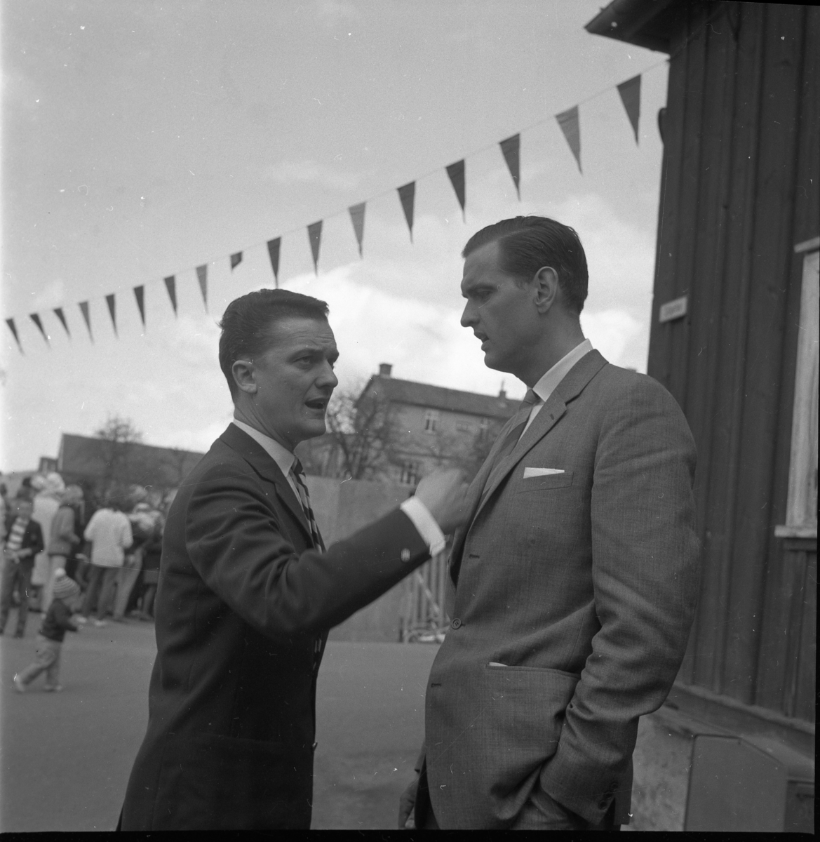 Lions vårmarknad 1964. Hans Roman och Rolf von Otter står på Sjögatan bakom Hallska gården och pratar. Roman gestikulerar med högerarmen.