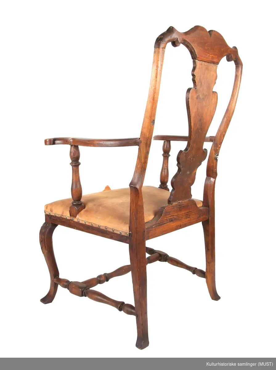 En stol med åpen rygg med symetrisk kontursaget ryggbrett.  Toppstykket har skåret skjell med blad. Sargen har samme dekor som toppstykket. Svungne forbein med skåret blad.
 Dette gjelder også midtfjølen.