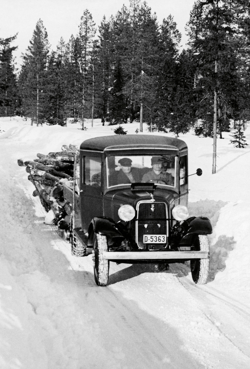 Transport av tømmer med lastebil.  Lastebilen er fotografert forfra på snødekt veg i landskap med furuskog.  To menn i førerhuset.  Bilen har lass på planet og på en etterhengt slede.  Kartotekkortet har ingen informasjon om opptakssted, men lastebilen er D-registrert (Hedmark) fylke, og vi har grunn til å tro at bildet er fra Elverum. 

Lastebilen er en Ford 1934-modell med et norskbygd førerhus med uvanlig høye vinduer. I 1935 var kjøretøyet (D-5363) registrert på P. og O. Rønningen fra Hernes i Elverum.
