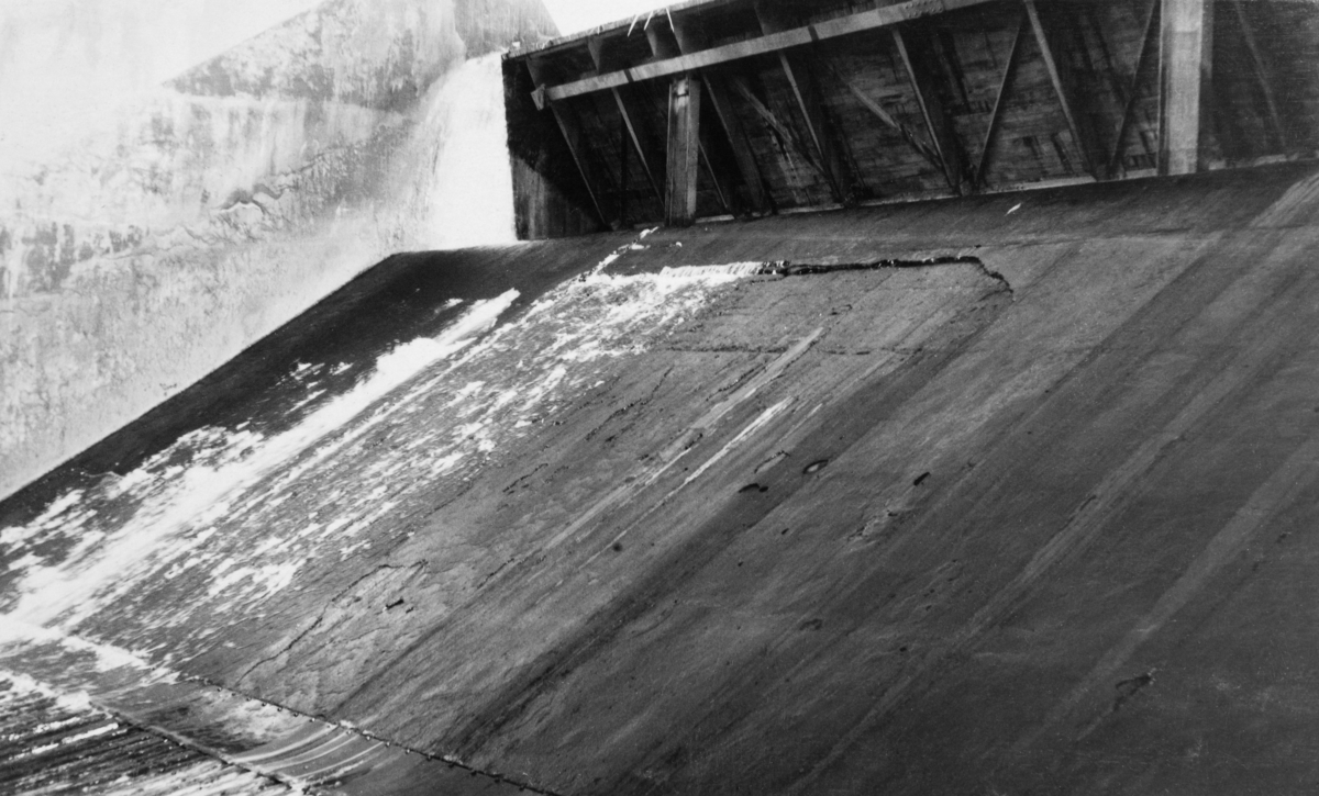 Detalj fra tømmerløpet i kraftverksdammen som ble bygd ved Osfallet i elva Søndre Osa i Åmot kommune i Hedmark.  Fotografiet er tatt i september 1915, et snaut år etter at kraftverket ble satt i drift.  På opptakstidspunktet var det åpenbart liten vanngjennomstrømming i elva, slik at en lett kunne se den glatte betongen som bare delvis var dekt av et tynt vannslør.

Osdammen ble ødelagt under vårflommen i 1916, og dambruddet forårsaket store skader på det nye anlegget, noe som innebar betydelige økonomiske tap for utbyggerne, Åmot kommune.  Mer informasjon om kraftutbygginga ved Osfallet og det påfølgende dambruddet finnes under fanen "Opplysninger".