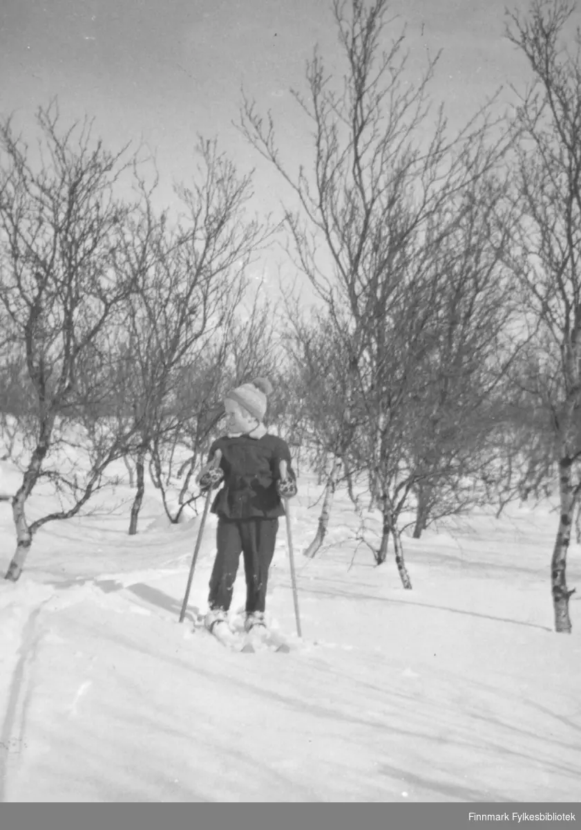 Liten skiløper fotografet i skiantrekk med ski på beina. Strikkelue og votter. Familiealbum tilhørende familien Klemetsen. Utlånt av Trygve Klemetsen. Periode: 1930-1960.