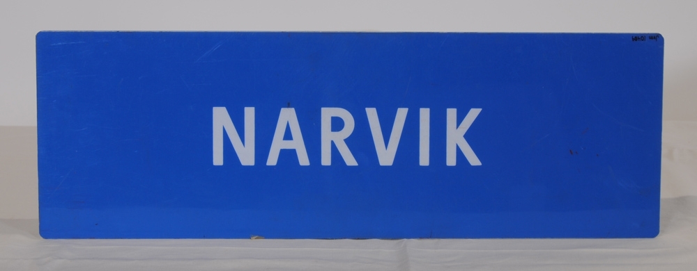 Destinationsskylt av ljusblå plast med texten "JÖNKÖPING-NÄSSJÖ NÄSSJÖ-JÖNKÖPING" i vitt på ena sidan. På motstående sida står det "NARVIK".