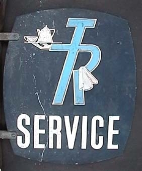 Dubbelsidig skylt av aluminium med vit och ljusblå tryck på mörkblå botten: "TR SERVICE"
Skylten skall sitta 90 grader ut från en vägg och är därför försedd med väggfäste.
Bottenfärgen är mörkblå. En ljusblå 'TR-pojke', Trafikrestaurangers logga, bär på kaffebricka och handduk
i vitt. Text i nederkant: "SERVICE" i vitt.

Skylten har lätt bågformade sidor.