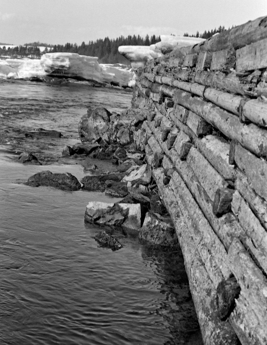 Deler av skådam, oppført i steinfylt tømmerkistekonstruksjon, i Bingsfossen i Sørum kommune i Akershus.  Fotografiet ble tatt i 1963, tidlig på våren mens vannstanden var lav.  I bakgrunnen lå det fortsatt digre is- og snøflak, og vannstanden Glomma var lav.  Skådammen - en ledeskjerm for fløtingstømmeret - var laftet som ei rektangulær kiste på berggrunnen.  Den hadde en del tverrstokker, som, når konstruksjonen ble fylt med stein fra elvefaret, bidro til at de sto støtt til tross for press fra flomvann og tømmer.