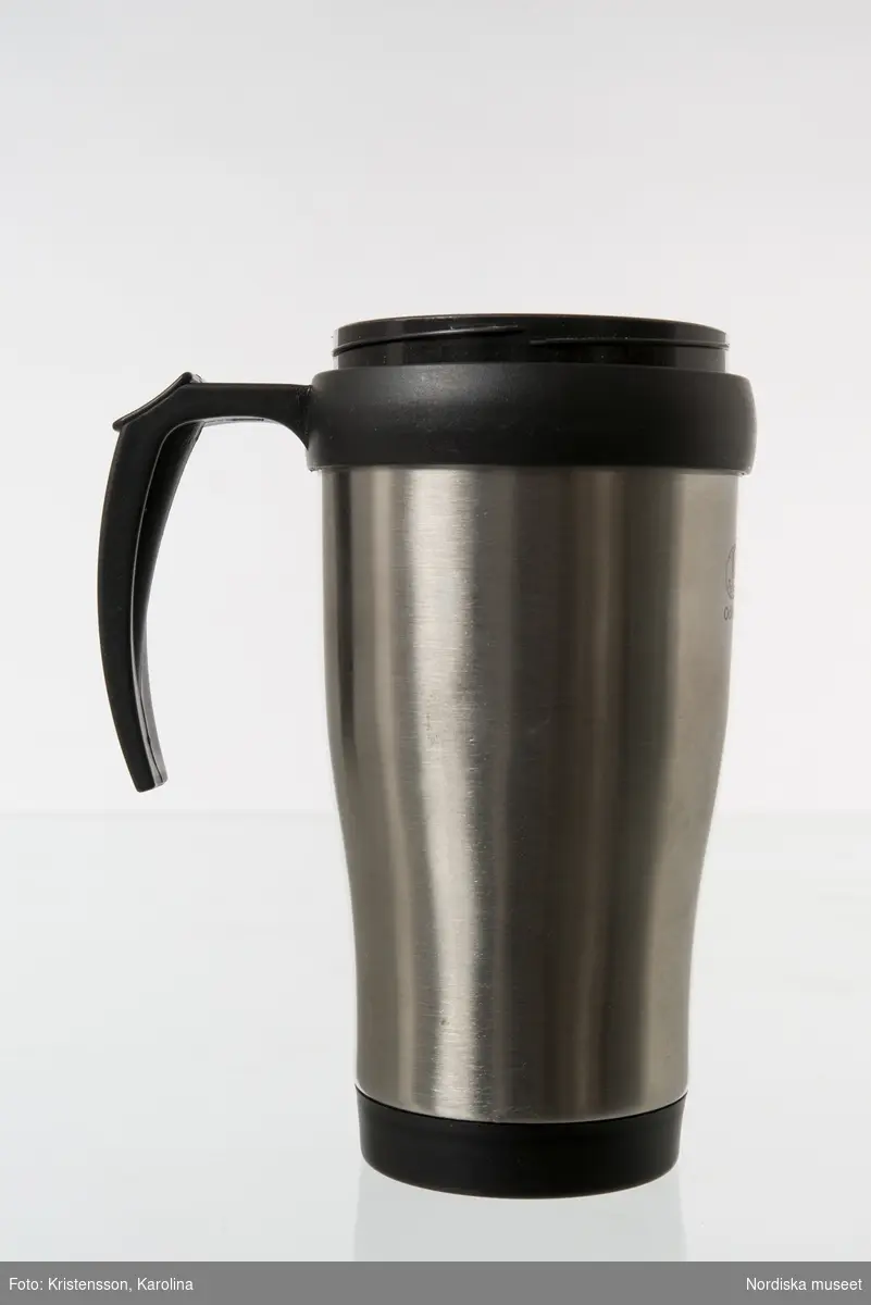 Termomugg av plast, med ytterhölje av aluminium. Används för varma drycker som kaffe och te. Locket saknas.