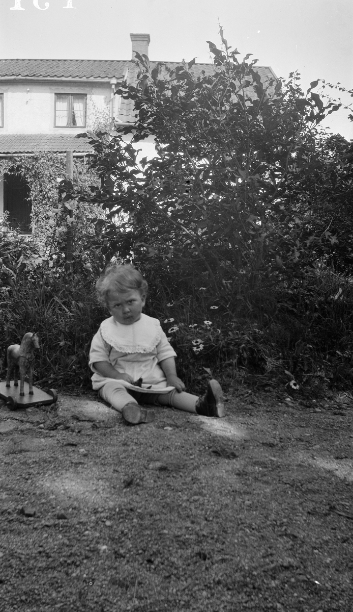 Litet barn sitter i trädgården, Uppland 1927