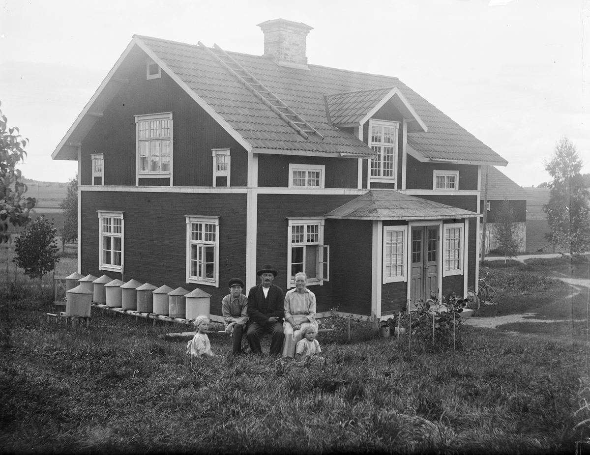 Familj framför bostadshus med bikupor i Sävasta, Altuna socken, Uppland 1925