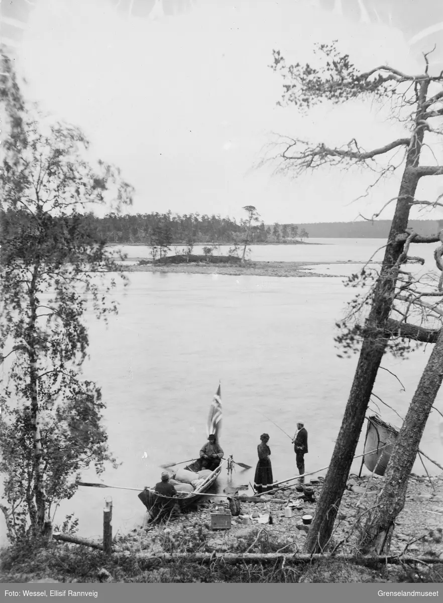 Rast ved elvebredden på tur til Vaggetem, juli 1897. Cand. jur. Hillestad fisker og Frk. Hagemann står ved siden av, to ukjente menn sitter i båten.