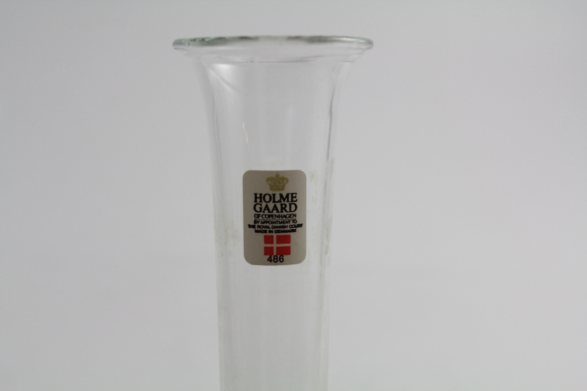 Sylindrisk glass, lett svunget ved fot og topp. Luftboble i bunnenes glassmasse. Klistermerke i toppen av glasset med logo og dansk flagg.