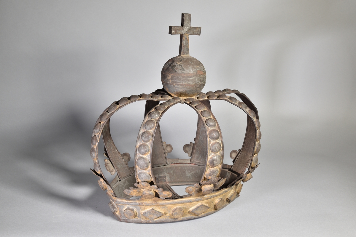 Skylt, oval, i form av tredimensionell krona med 8 bågar och krönt med klot och kors. Rester av färg.