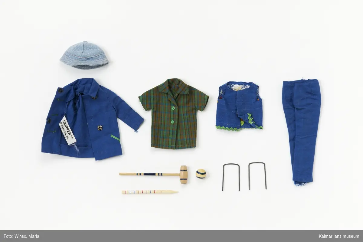 KLM45643:5 Dockdräkt, jacka, byxor, skjorta, väst, hatt och krocketspel. Jacka, blått tyg med gröna knappar och gröna dekorationer vid knappar och fickor, tryckknappar. Byxor, blått tyg med tryckknapp i midjan. Skjorta, rutig i grönt, blått och brunt med gröna knappar, kort ärm. Väst, av blått tyg kantad med grönt veckband nertill och med broderi med hjärta, fåglar och blommor på ryggen samt tryckknappar fram. Solhatt, av ljusblått tyg. Krocketset med klubba, två bågar av metall, pinne av trä och klot av trä. Blåa ballerina skor av plast med texten ”JAPAN” på sulan. Jackan märkt med Mattels etikett. Setet finns i häftet ”Barbie och hennes vänner – med många nya kläder” från Brio och heter ”920 Fun time”. Setet är för Skipper.