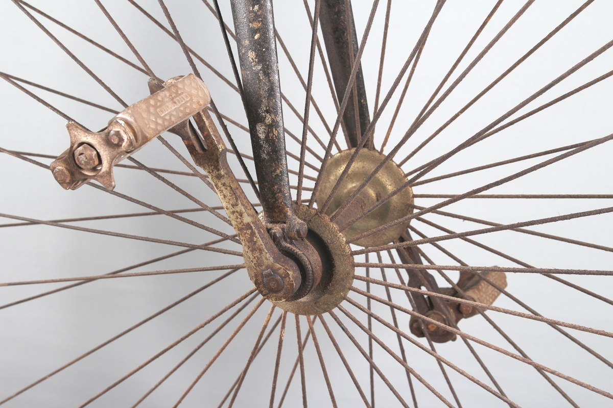 Svartlakkert velosiped med stort forhjul og lite bakhjul. Pedalene er montert direkte på fornavet og setet er plassert rett over.