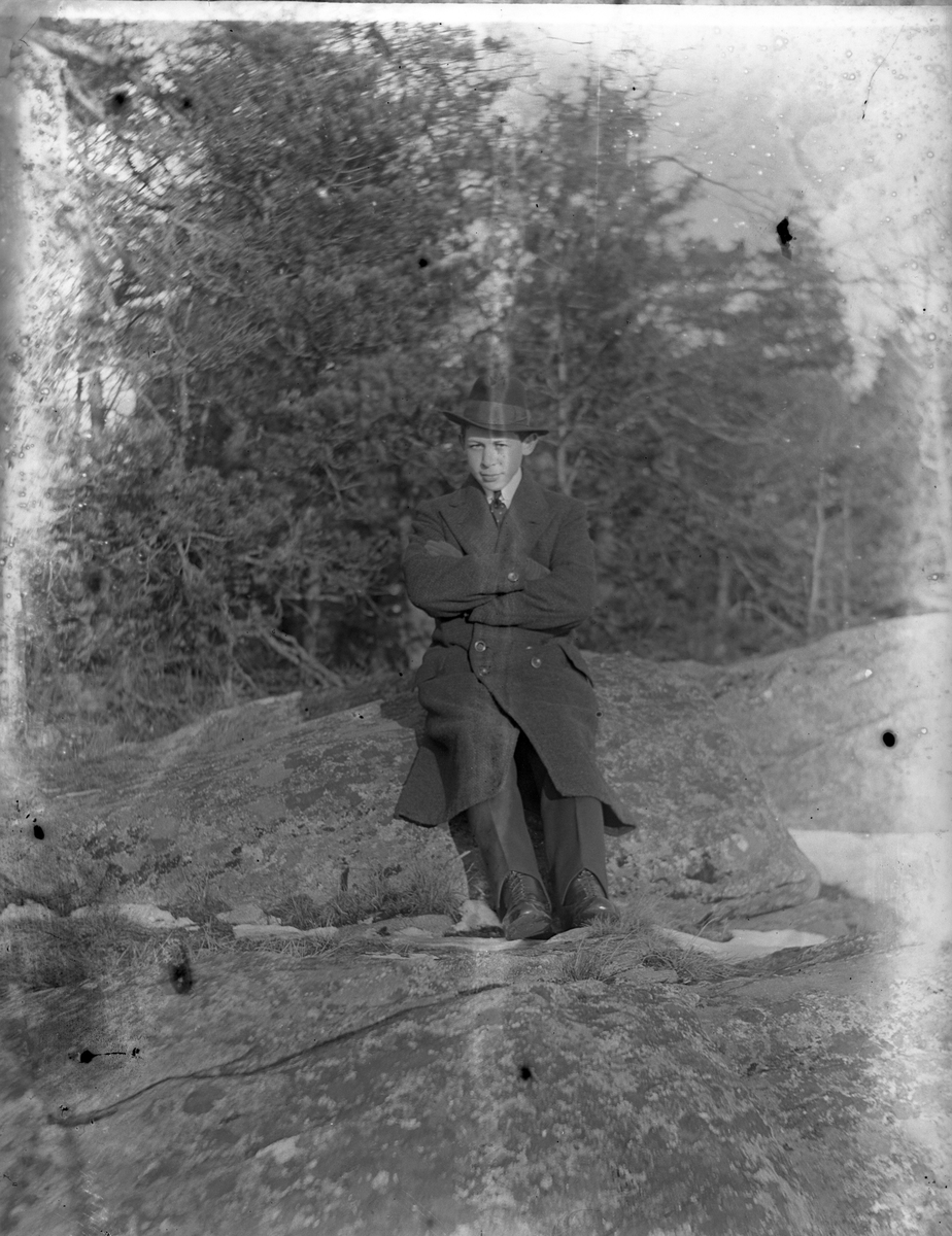 Hugo Larsson i hatt och rock sitter på en sten och tittar in i kameran.