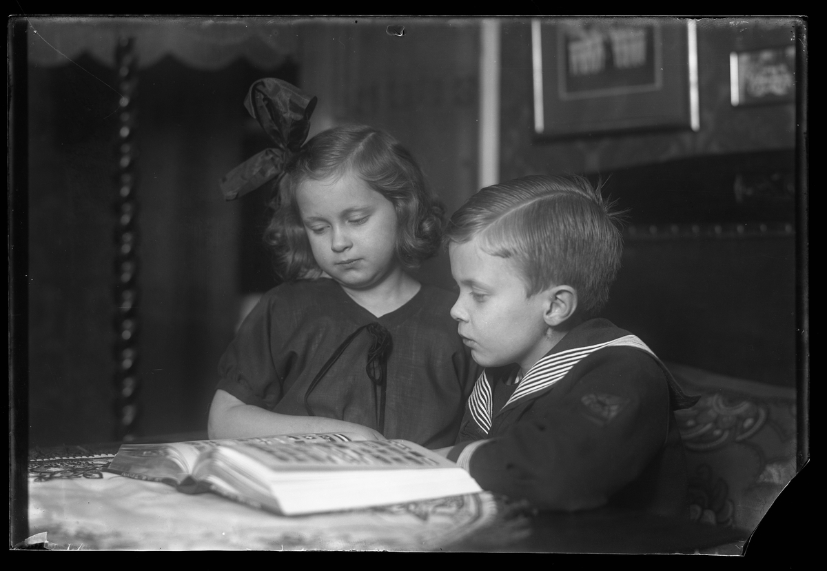Syskonen Gerd Anna-Lisa Nilsson och Bengt Fredrik Nilsson sitter vid ett bord och tittar i en bok.