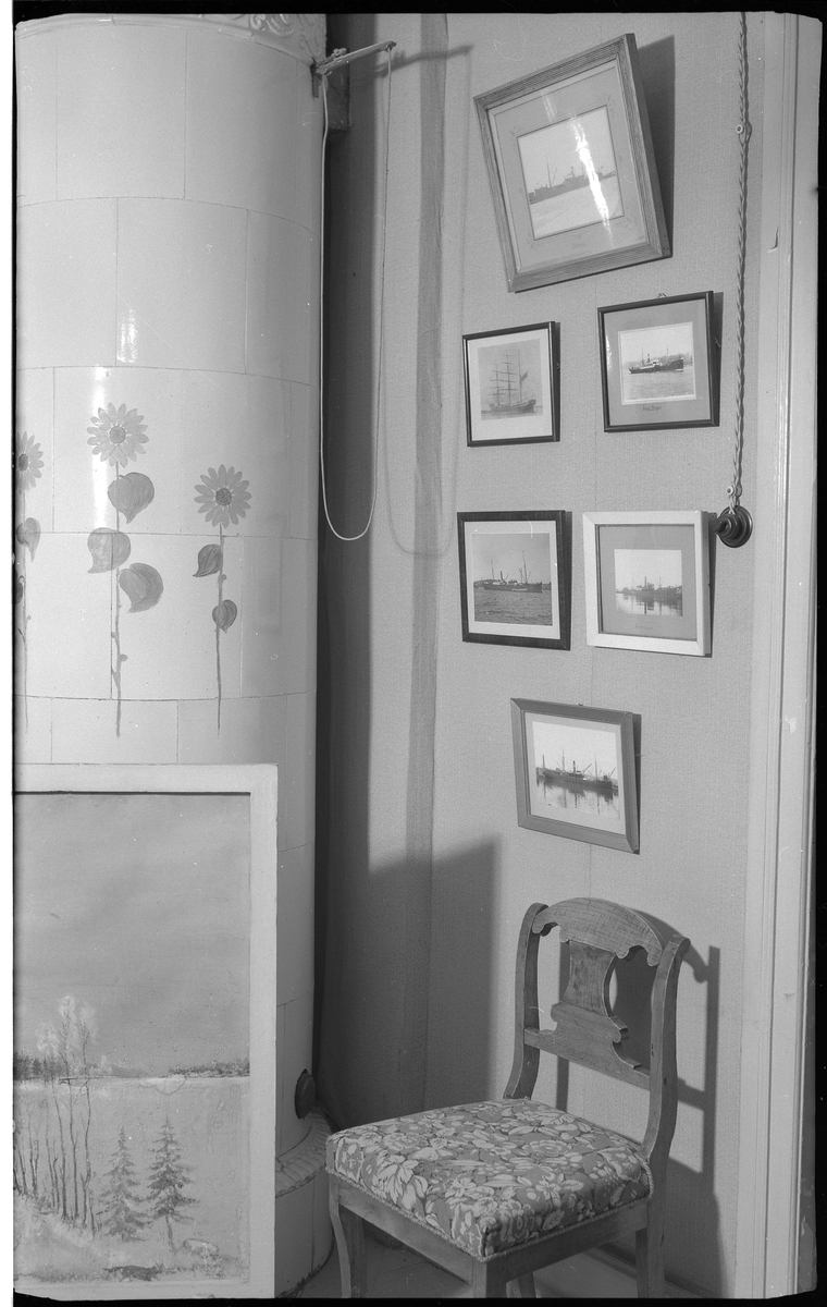 Interiör från en äldre bostadshus, villa Charlottenberg (Hedvigsberg) vid Göteborgsvägen. Huset byggt på 1800-talet.
I ett hörn står en rund kakelugn, vit med stiliserade blommor målade på mitten.
Ovanför en stol med klädd sits, hänger sex tavlor, framför kakelugnen syns en del av en större tavla.

Villa Charlottenberg (Hedvigsberg) på Göteborgsvägen.

Elin Bothén.

Foto 13 september 1966.
