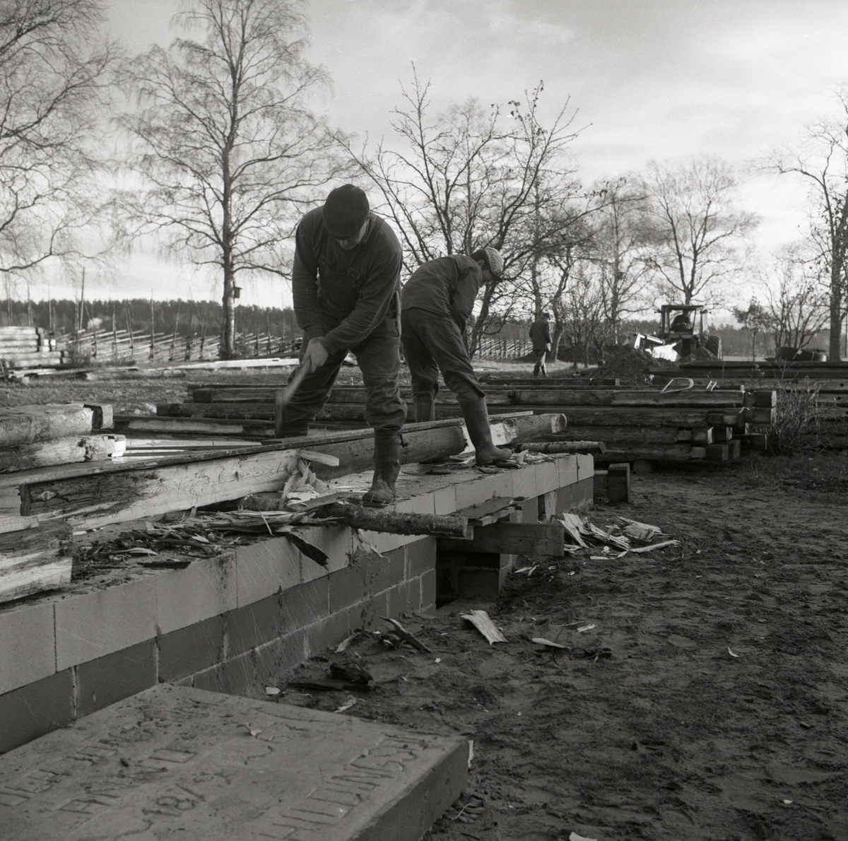 Två män justerar timmerstockar med yxa vid byggnation av ett bostadshus vid gården Sunnanåker, 1967.