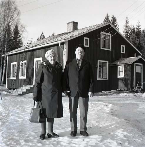 En kvinna och en man poserar framför ett hus i vinterskrud, 1972.