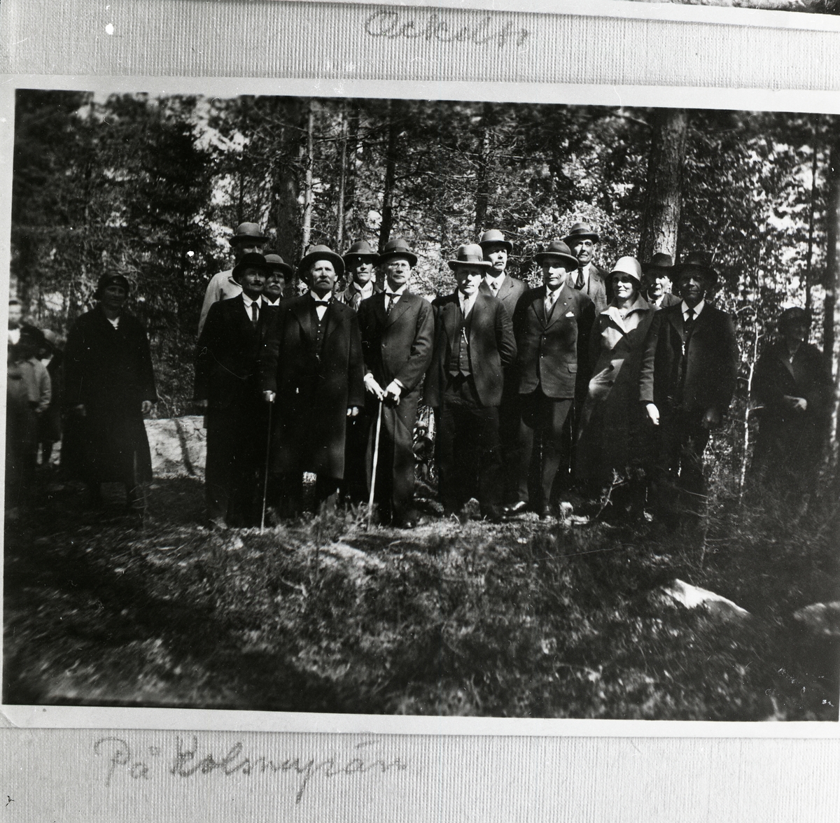 En grupp män iklädda kostym och hattar står ute i skogen.