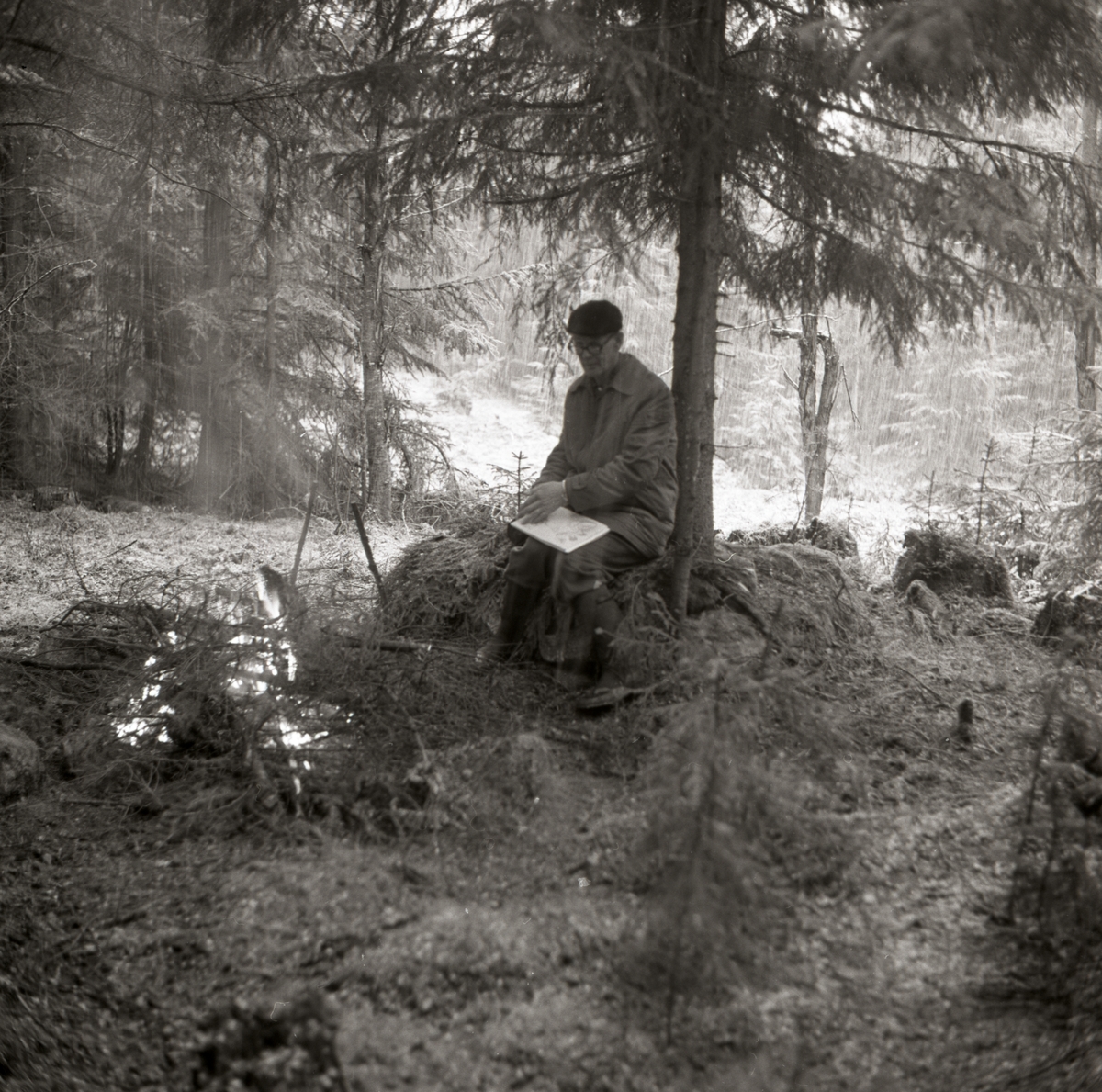 En man sitter och beskådar ruiner i Västerby. Han har tänt en lägereld och i hans knä vilar ett ritblock, 5 maj 1968 i Rengsjö.