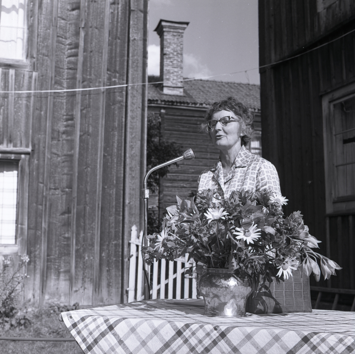 En kvinna står vid en mikrofon och håller ett tal under hembygdsfesten, 1962 i Rengsjö.