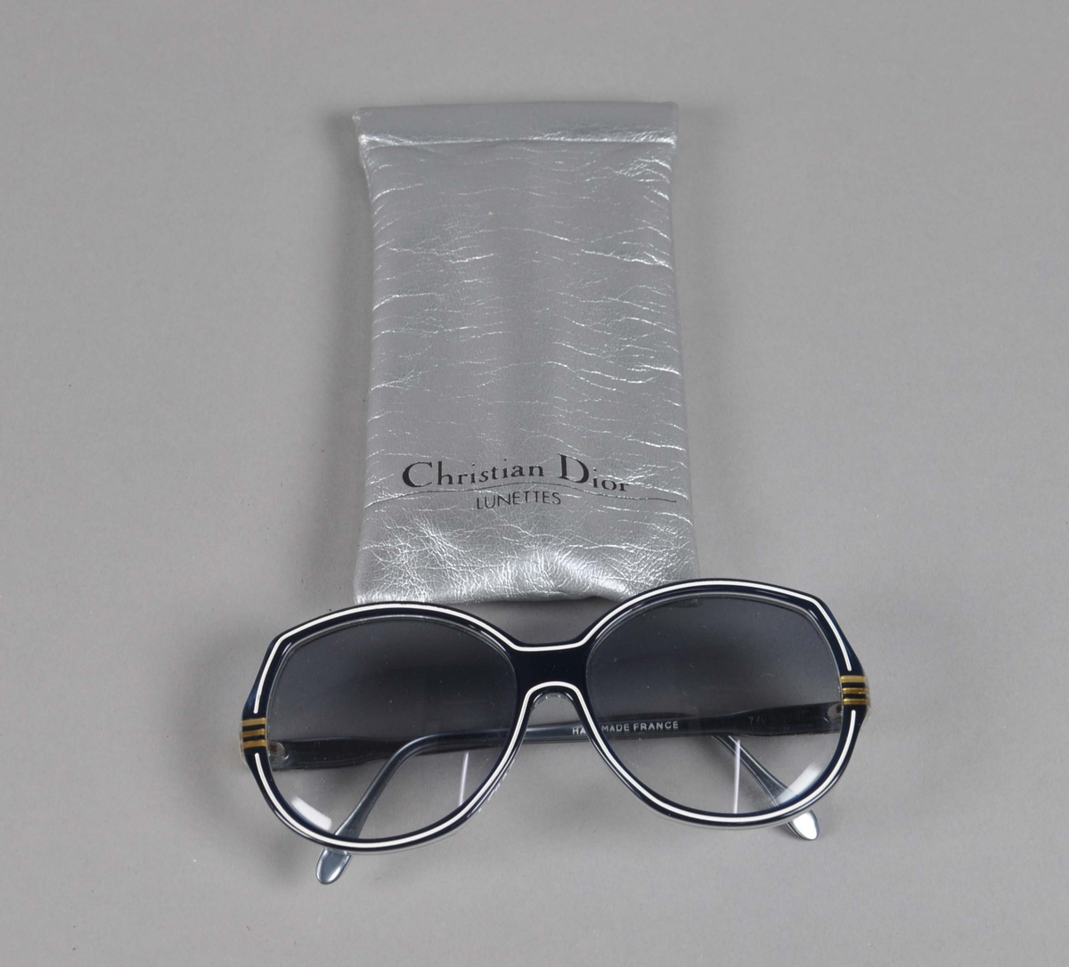 Sølvfarget brilleetui av tekstilt materiale. I etuiet er det et par solbriller.