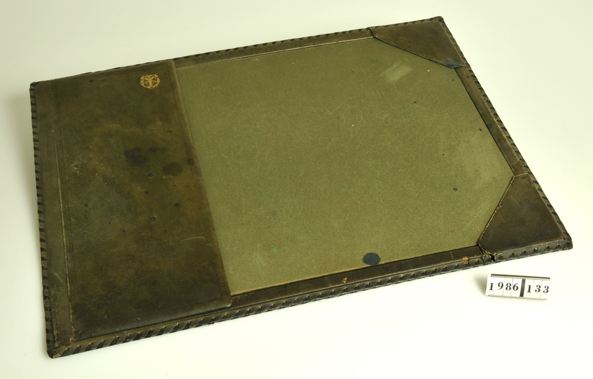 Grön. Klaff med vapen i guld med initialerna TMB.
Laskade kanter. Baksidan klädd med filt. Läskpapper.
Kalender från 1940.
