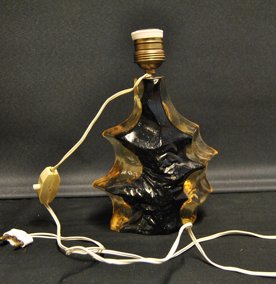 Lampe med uregulær form. Støpt i lucite recin akryl. Støpt i plasen er korall, sjøhest, krabbe og skjell. Er mest sannsynlig fra 1960-1980- årene. Mulig souvenir fra Spania.