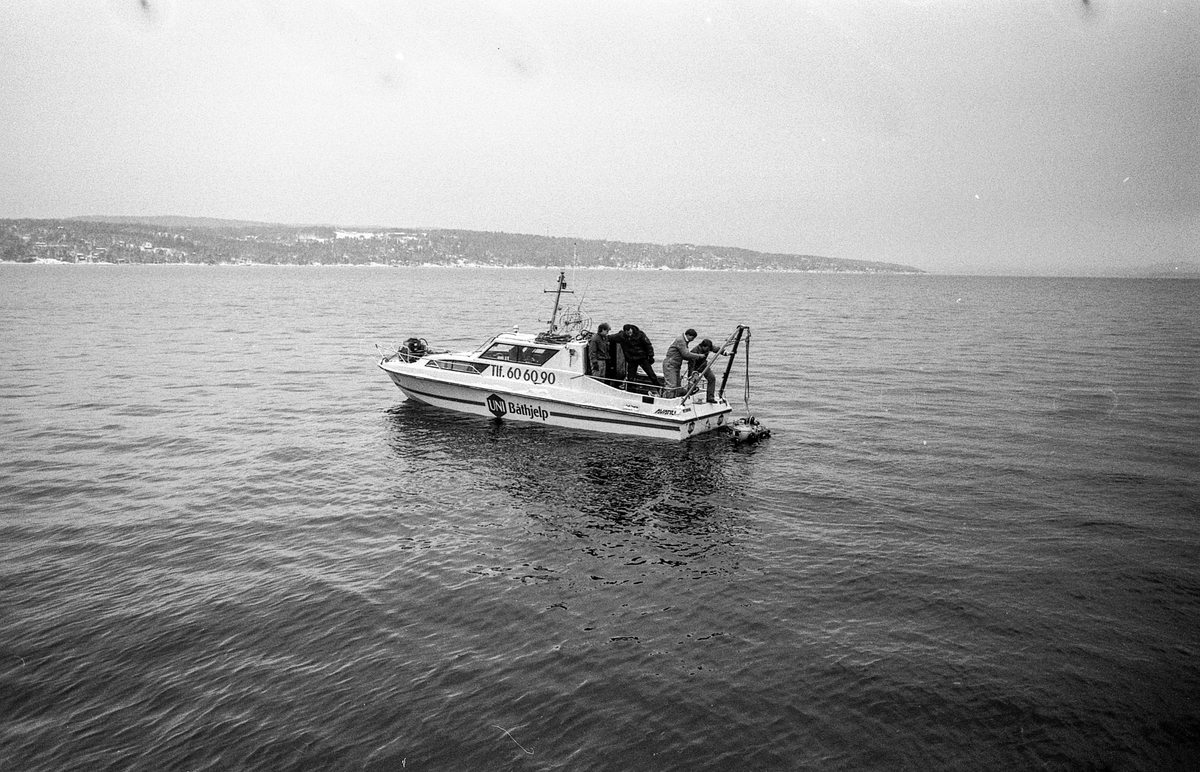 Miniubåtjakt etter dumpede biler og motorsykler i Oslofjorden utenfor Oppegård. Menn i kjeledress og strikkeluer håndterer miniubåten fra større båt, cabincruiser.