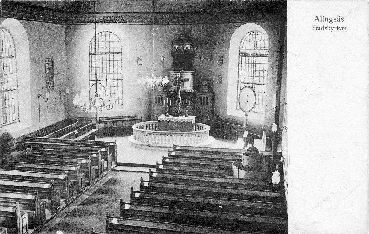 Vykort med bild på interiör från Alingsås Stadskyrka sedd ovanifrån med predikstol och altare i centrum på bilden och bänkar utmed sidorna.