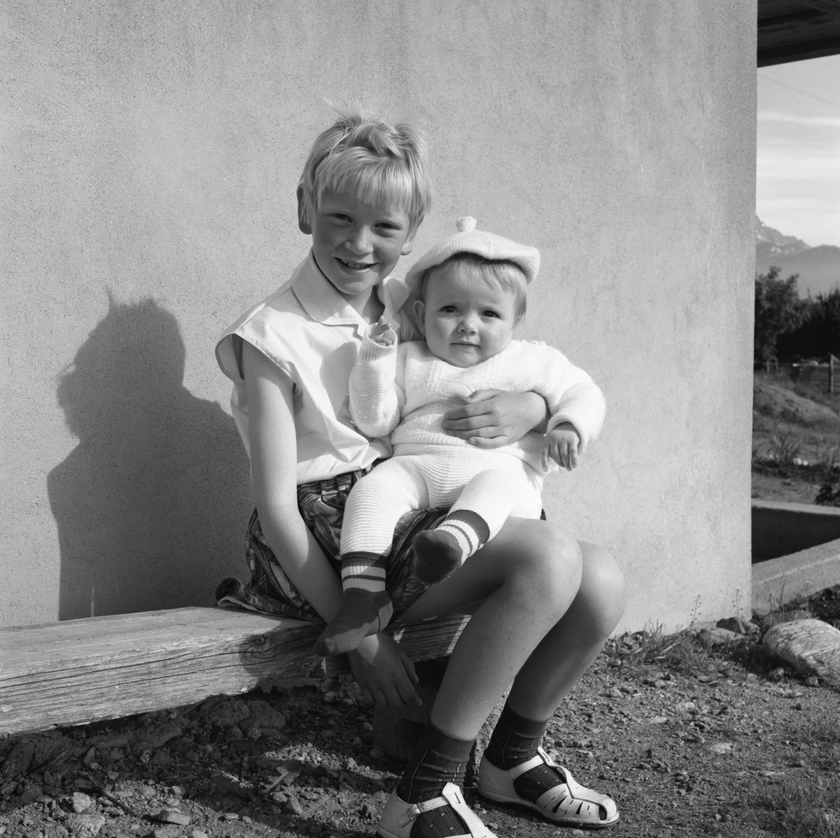 Portrettfotografi av ei jente med en baby på fanget utenfor et hus. Bjørg og Frode?