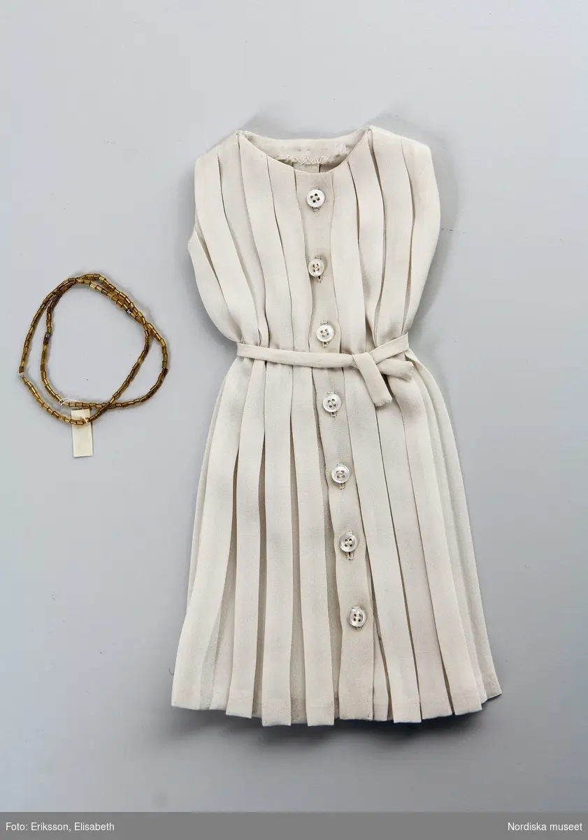 Katalogkort:
c) klänning, plisserad, vit; halsband