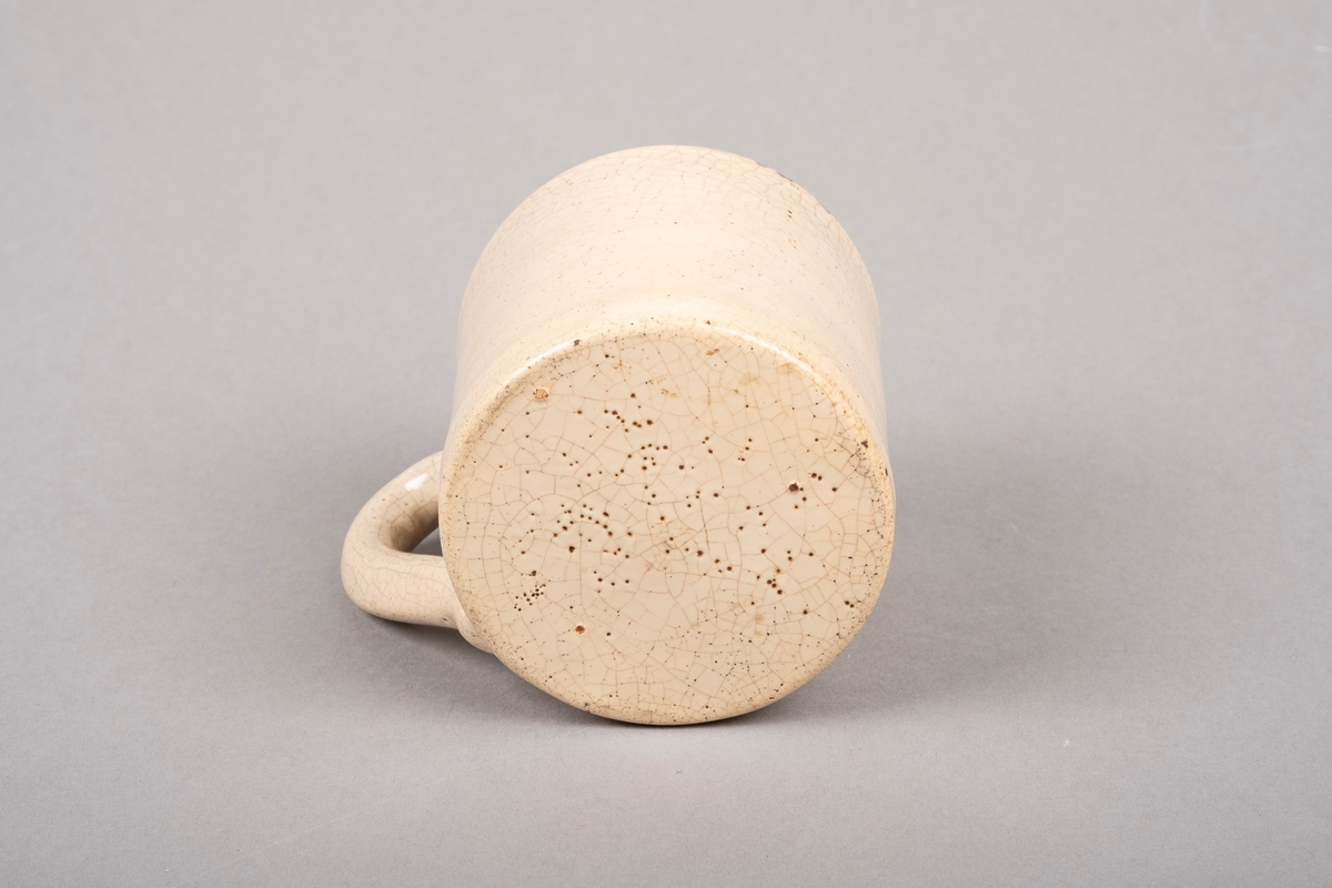 Keramikkopp med hank. Koppen er lakkert med beigefarget glasur. Det er krakeleringer på på hele koppen.