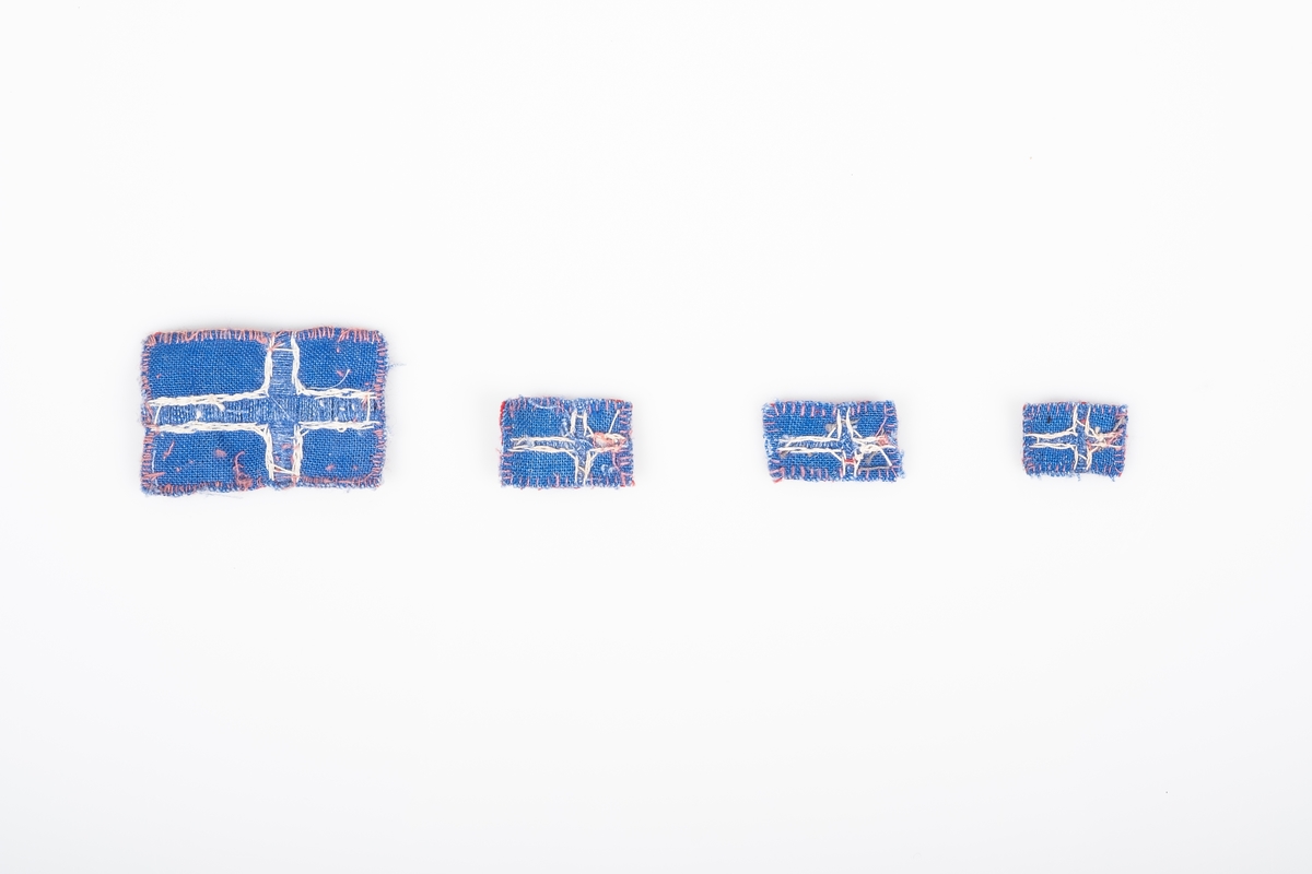 Fire små norske flagg. Flaggene er i ulike størrelser. De er sydd og brodert på hånd. De er sydd sammen av to stoffbiter, rød på forsiden og blå på baksiden. Det blå og hvite krysset på flagget er brodert.